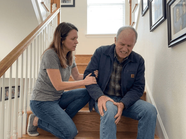 Older man sitting on stairs, holding his knee in pain
